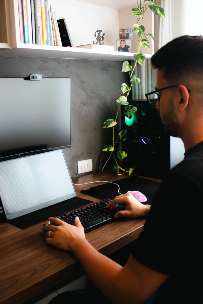 Young man at a home office desk with a laptop and an external monitor, working through records on screen