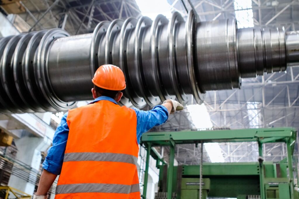 Engineer in a hard hat and high-visibility vest inspecting machinery in a factory