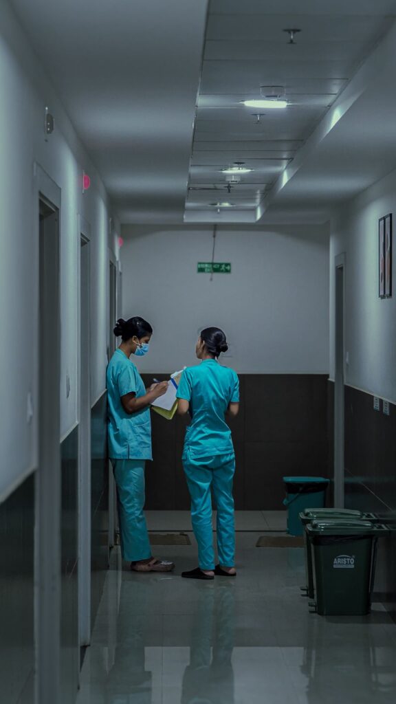 Two nurses in scrubs reviewing patient notes in a hospital corridor