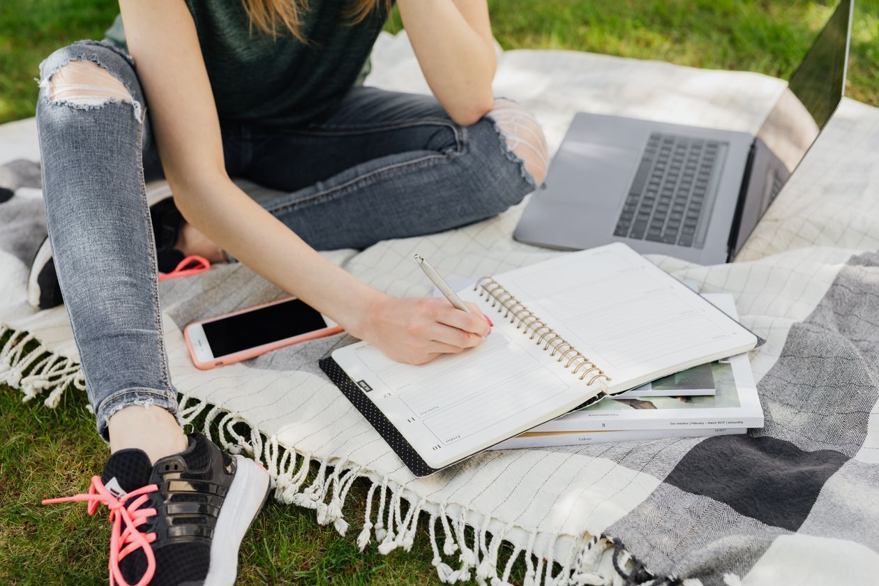Student preparing for an English language proficiency test with notebook and laptop outdoors