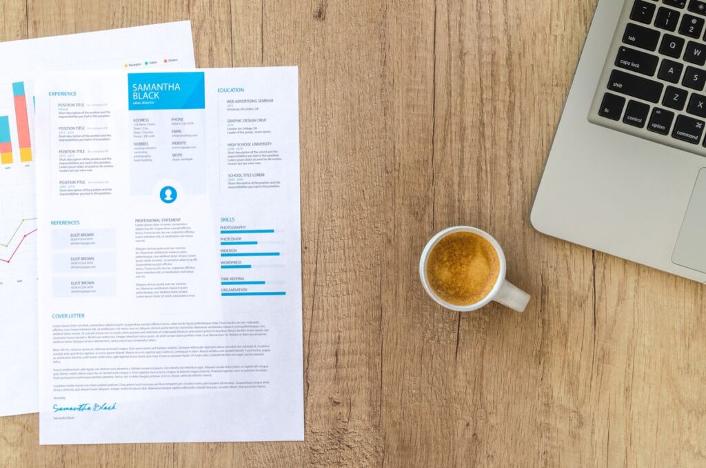 A printed CV, laptop and coffee cup on a wooden desk, ready for an online job application