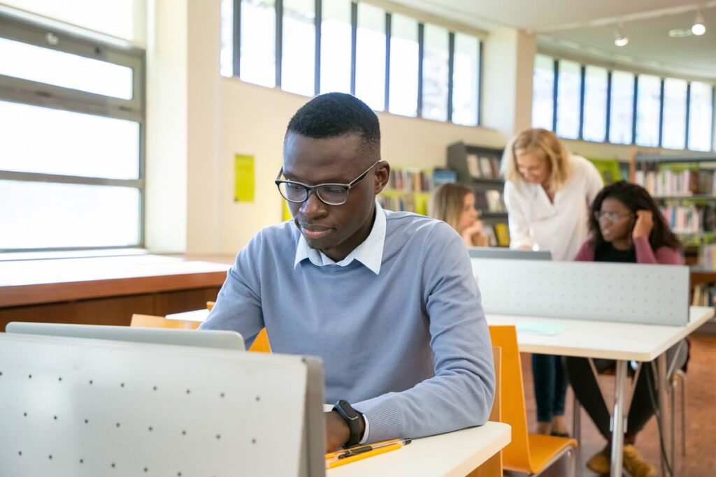 Student in glasses working on a laptop at a classroom desk, preparing documents for a graduate school application
